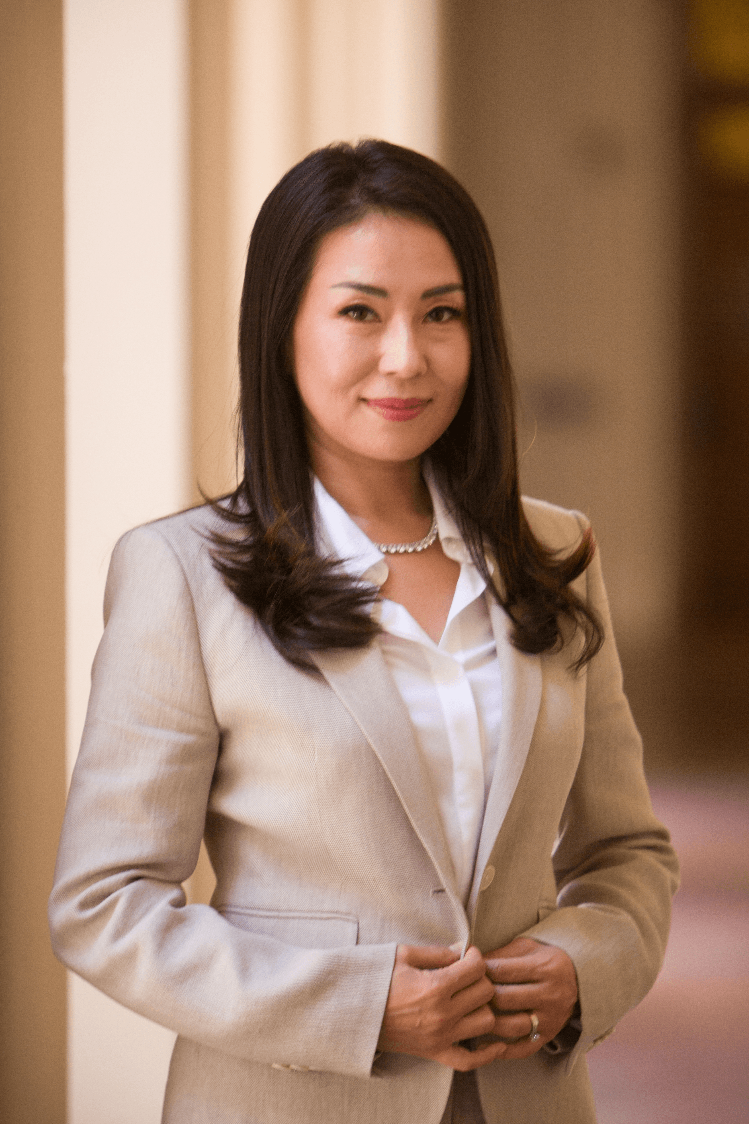 Attorney Michelle Choe in a beige suit, smiling in a sunlit colonnade